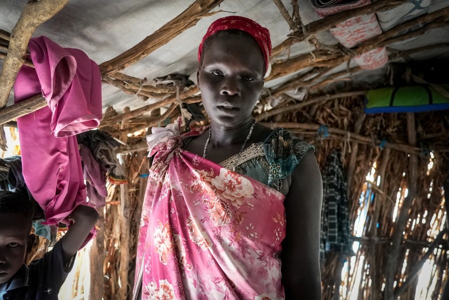 Nyarok Gach, who fled Sudan after fighting erupted and returned to her home village in South Sudan earlier this month, stands in a house that she shares with her eight children and other families, at Wunlueth village in Canal-Pigi county, South Sudan Thursday, May 4, 2023. More than 40,000 people, mostly South Sudanese, have crossed the border into South Sudan since Sudan erupted in conflict nearly one month ago, yet many are returning to areas unable to support them and still riddled by fighting. (AP Photo/Sam Mednick)