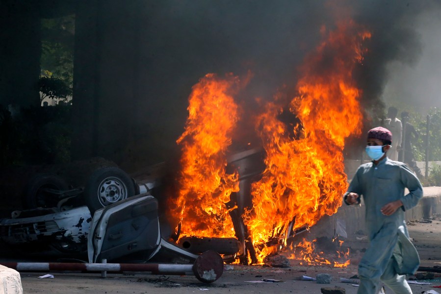 A man runs past a burning car set on fire by angry supporters of Pakistan's former Prime Minister Imran Khan during a protest against the arrest of their leader, in Peshawar, Pakistan, Wednesday, May 10, 2023. A court has ruled that former Pakistani Prime Minister Imran Khan can be held for questioning for eight days. The decision Wednesday comes a day after the country’s popular opposition leader was dragged from a courtroom and arrested. His detention set off clashes between his supporters and police Tuesday. (AP Photo/Muhammad Sajjad)