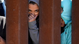 Migrants waiting to apply for asylum between two border walls look through the wall Thursday, May 11, 2023, in San Diego. Pandemic-related U.S. asylum restrictions, known as Title 42, are to expire May 11. (AP Photo/Gregory Bull)