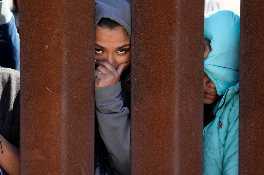 Migrants waiting to apply for asylum between two border walls look through the wall Thursday, May 11, 2023, in San Diego.