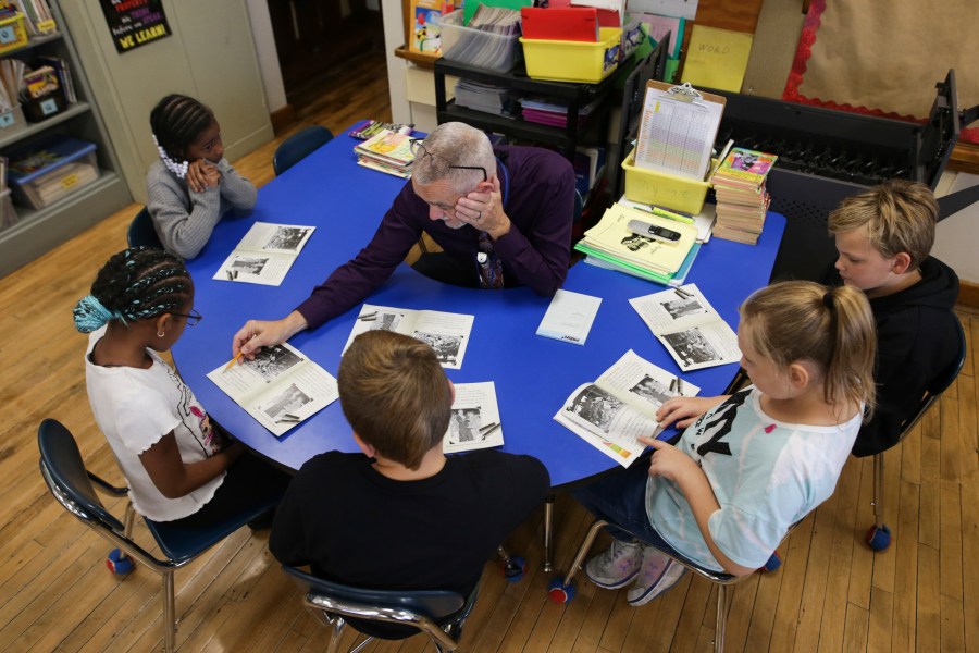 Richard Evans, a teacher at Hyde Park Elementary School, helps Ke'Arrah Jessie sound out a word during a reading circle in class on Thursday, Oct. 20, 2022, in Niagara Falls, N.Y. Evans calls a handful of students back for extra help in reading — a pivotal subject for third grade — at the end of each day.