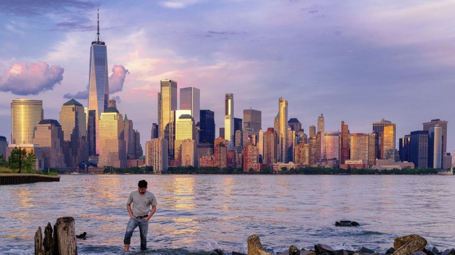 FILE — A man checks his footing as he wades through the Morris Canal Outlet in Jersey City, N.J., as the sun sets on the lower Manhattan skyline of New York City, May 31, 2022. If rising oceans aren't worry enough, add this to the risks New York City faces: The metropolis is sinking under the weight of its skyscrapers, apartment buildings, asphalt and humanity itself — and will eventually become flooded by the Hudson River and Atlantic Ocean. (AP Photo/J. David Ake, File)