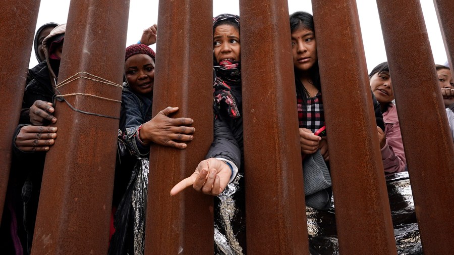 Migrants reach through a border wall for clothing handed out by volunteers, as they wait between two border walls to apply for asylum Friday, May 12, 2023, in San Diego.