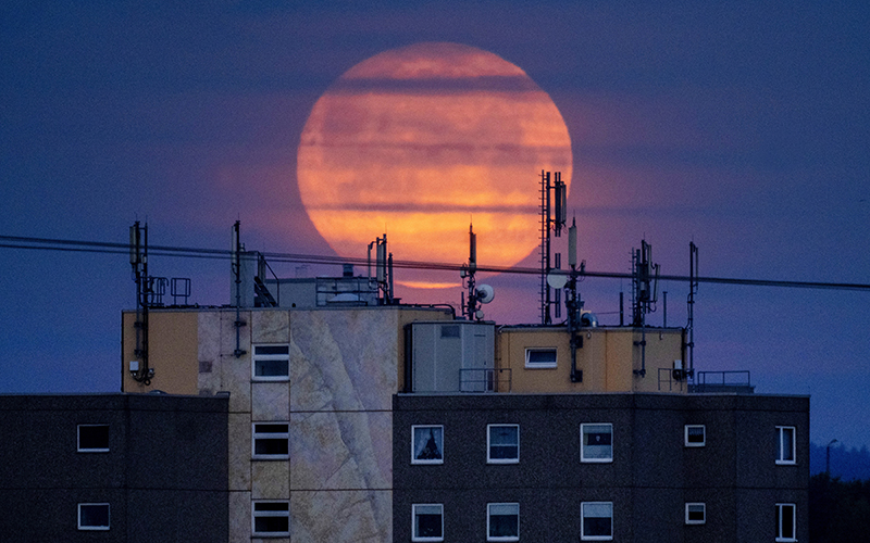 The full moon sets over an apartment building