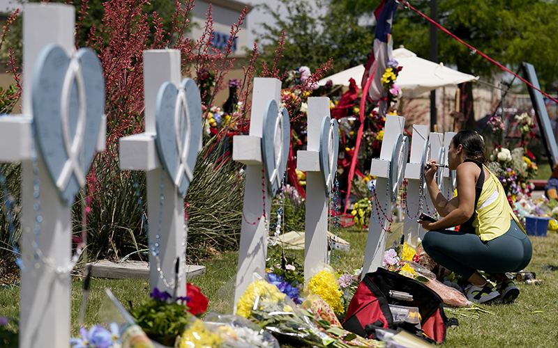 A woman signs a cross that stands alongside others at a makeshift memorial