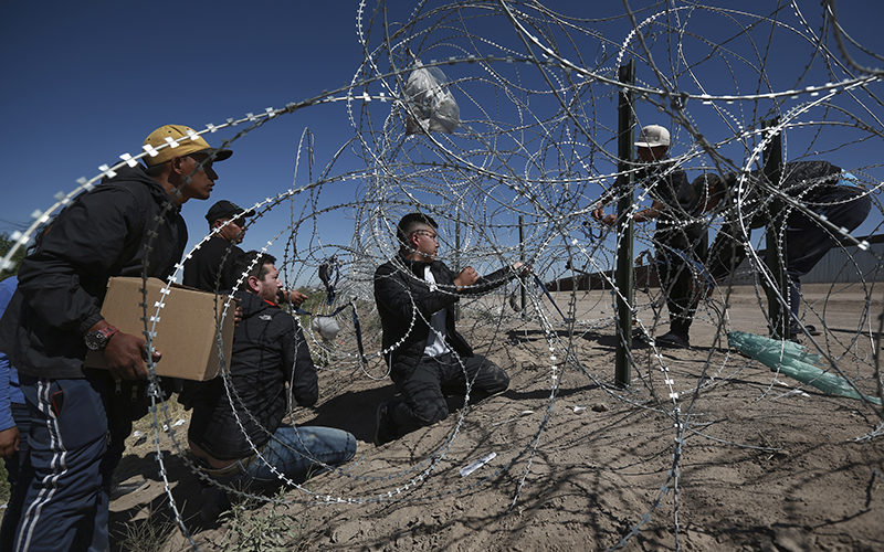 Migrants cross a barbed-wire barrier into the United States from Ciudad Juárez, Mexico