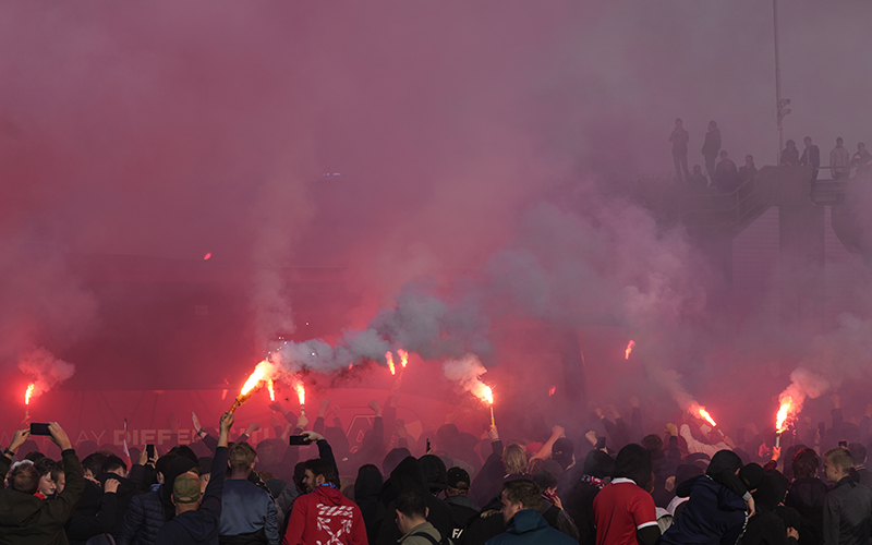 AZ supporters, some holding flares, meet the players' bus in a fog of red light