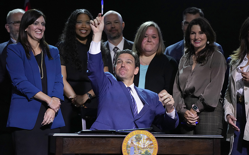 Florida Gov. Ron DeSantis (R) throws a marker into the audience at a bill signing as officials behind him watch