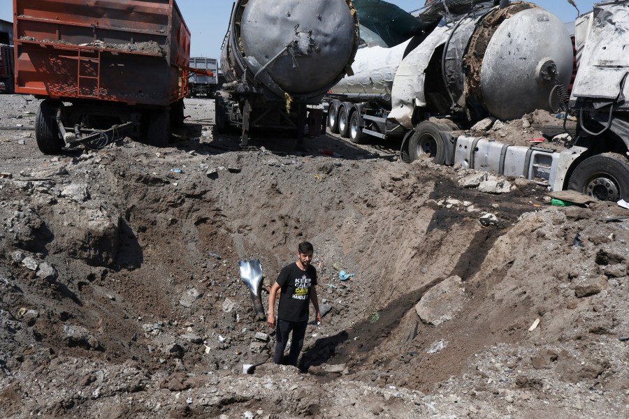 A man stands inside a crater next to destroyed trucks after Russian shelling in Rozumivka, near Zaporizhzhia, Ukraine, Tuesday, June 20, 2023. (AP Photo/Andriy Andriyenko)