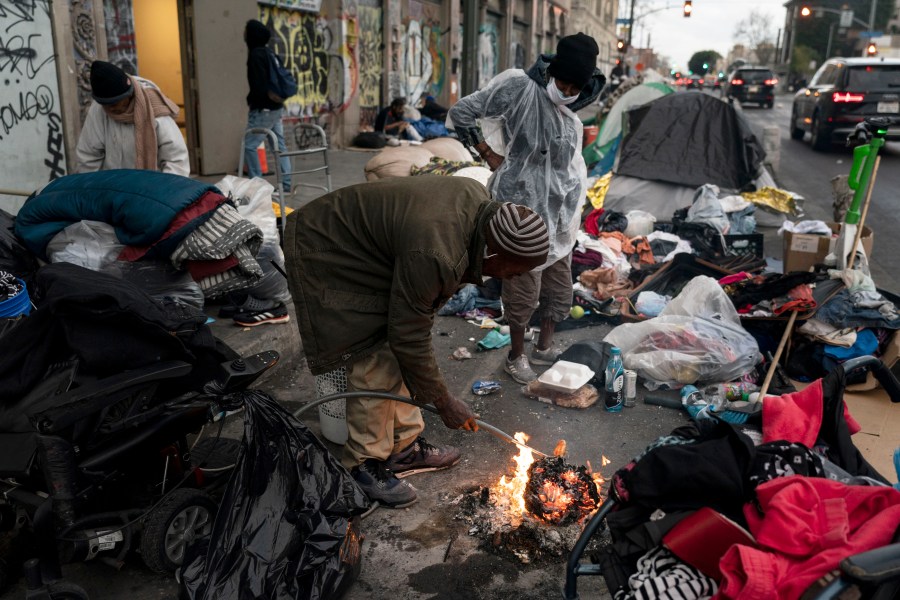 FILE - Robert Mason, a 56-year-old homeless man, warms up a piece of doughnut over a bonfire he set to keep himself warm on Skid Row in Los Angeles, on Feb. 14, 2023. The number of homeless residents counted in Los Angeles County spiked again, increasing by 9% since last year in the latest marker of how deep the crisis is of people sleeping in cars, encampments or shelters in California. (AP Photo/Jae C. Hong, File)