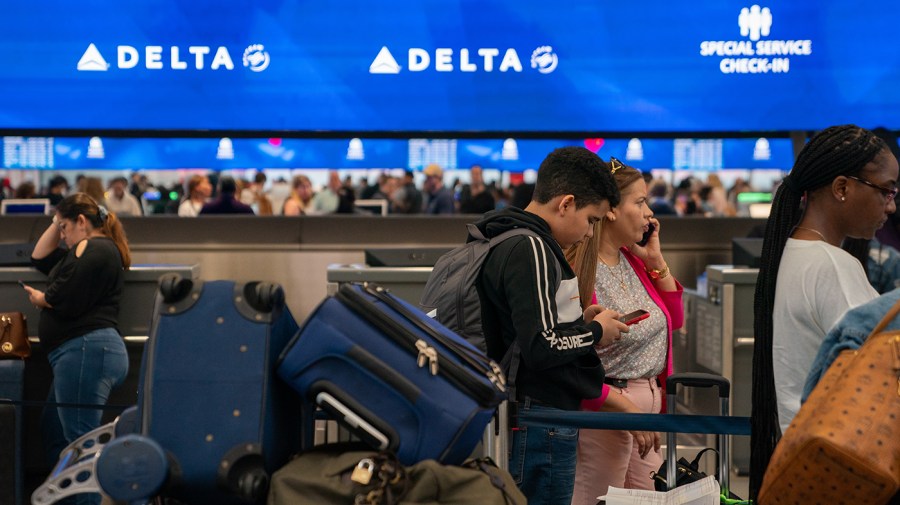 People line up with their bags in front of a blue Delta check-in banner in the background