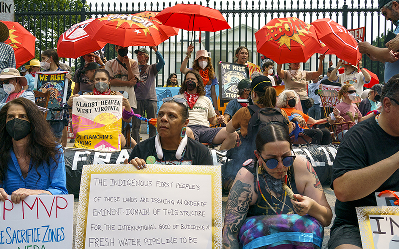 Protesters affiliated with People vs. Fossil Fuels demonstrate outside the White House, holding signs while some carry red umbrellas