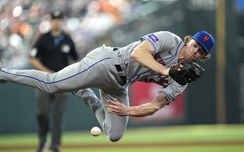 New York Mets pitcher Josh Walker throws to first. He is in the air, parallel to the ground with one leg bent, and the ball has just left his hand