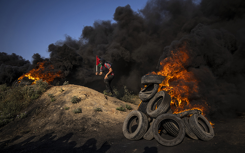 A Palestinian man stands between piles of burning tires and waves the national flag during a Monday protest