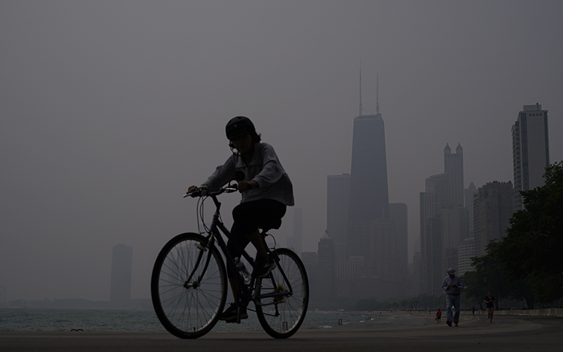 A person rides a bicycle along the shore of Lake Michigan as the downtown skyline is blanketed in haze