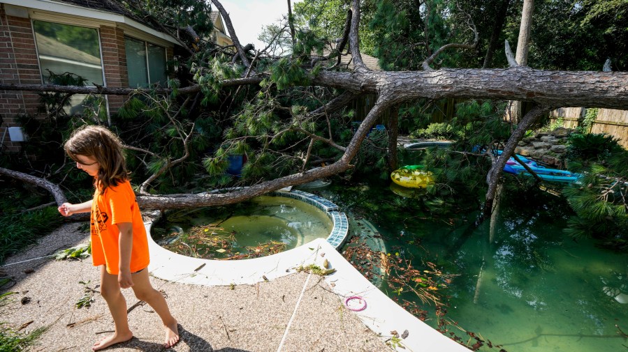 Bailey Hatfield walks past a toppled tree in the backyard of her home, Thursday, June 22, 2023 in Spring, Texas, after an overnight storm blew through the area, knocking out power and downing trees.