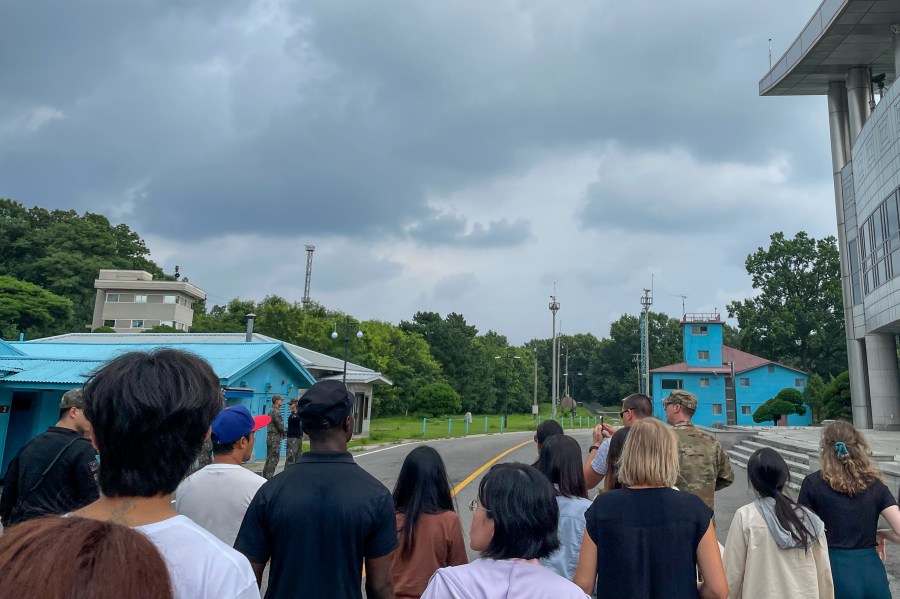 UPDATED CAPTION: A group of tourists stand near a border station at Panmunjom in the Demilitarized Zone in Paju, South Korea, Tuesday, July 18, 2023. Not long after this photo was taken, Travis King, a U.S. soldier, pictured with dark blue shirt and dark cap, fourth left, bolted across the border and became the first known American detained in the North in nearly five years. (AP Photo/Sarah Jane Leslie)