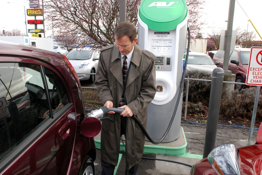 FILE - Thomas Miller, Western EV fleet sales manager for Mitsubishi Motors North America, demonstrates a fast-charger connection on a Mitsubichi i car Friday, March 16, 2012 in Central Point, Ore. The second-largest electric vehicle fast-charging network, Electrify America, with 800 direct-current fast-charging stations and more than 3,600 plugs nationwide, said Wednesday, July 26, 2023, it will work to add Tesla's connector to existing and future chargers by 2025. (AP Photo/Jeff Barnard, File)