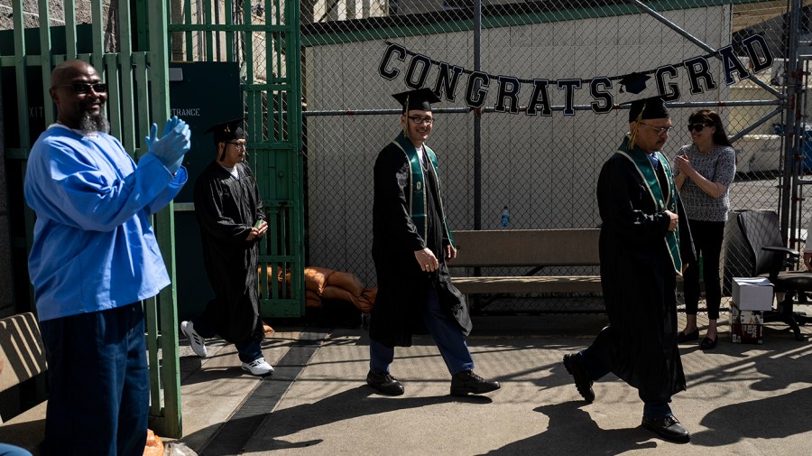 A prisoner applauds as Lambert Pabriaga, right, and Eric Pomatto, center, walk into their graduation ceremony at Folsom State Prison in Folsom, Calif., Thursday, May 25, 2023.