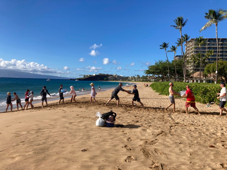 A group of volunteers who sailed from Maalaea Bay, Maui, form an assembly line on Kaanapali Beach on Saturday, Aug. 12, 2023, to unload donations from a boat. Maui residents have come together to donate water, food and other essential supplies to people on the western side of the island after a deadly fire destroyed hundreds of homes and left scores of people homeless. (AP Photo/Rick Bowmer)