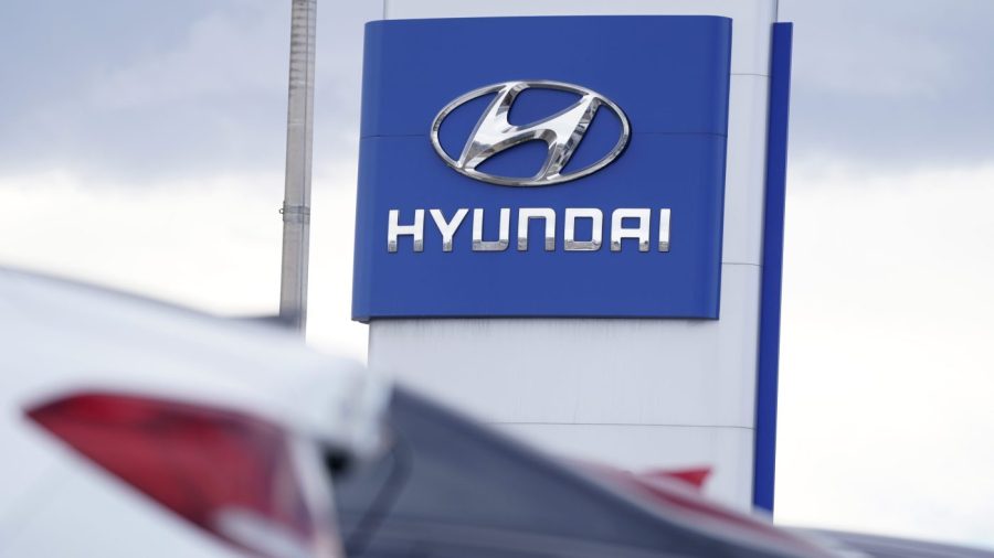 The Hyundai company logo is seen on a sign above a row of cars at a car dealership.