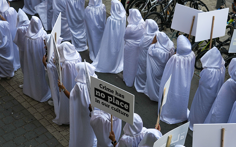 Palestinian citizens of Israel wearing long white robes with hoods protest over the spiraling rate of violent crime. One sign reads "Crime has no place in our culture"