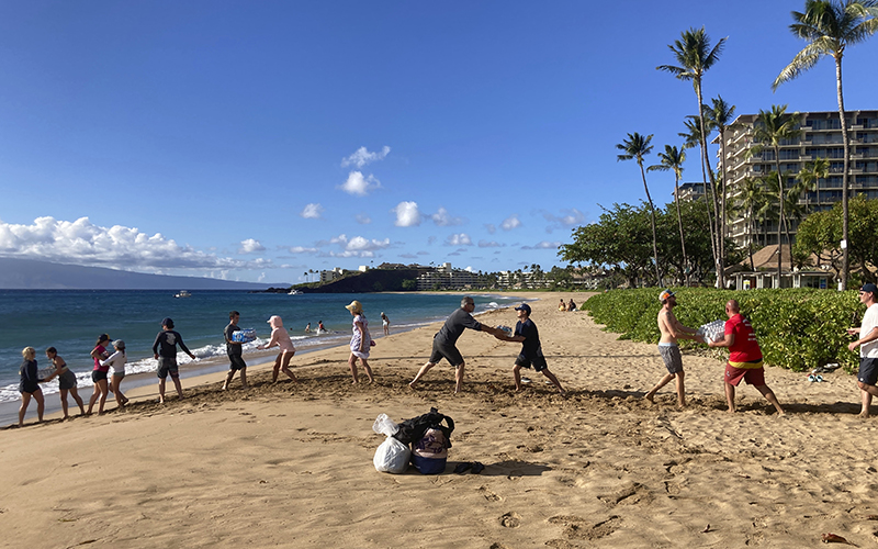 A group of volunteers form a line to pass emergency supplies from a boat up the beach