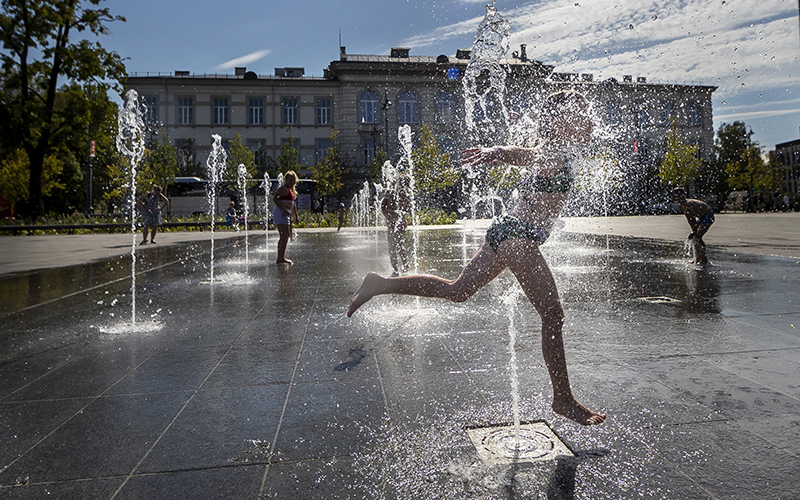 A girl splashes through a jet of water in a public fountain