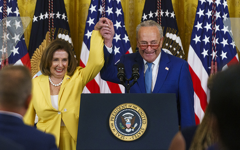 Rep. Nancy Pelosi (D-Calif.) and Majority Chuck Schumer (D-N.Y.) raise their held hands during a ceremony to mark the anniversary of the Inflation Reduction Act