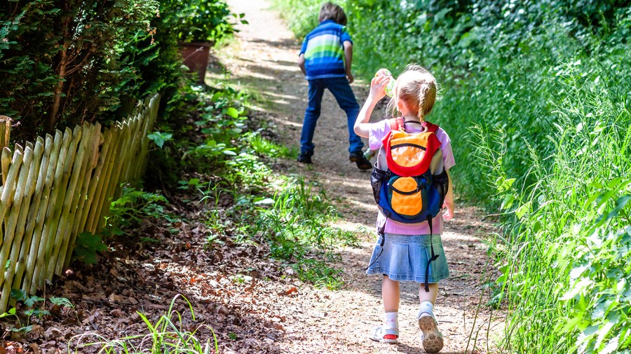 Little girl walking to school with backpack and drinking water out of a bottle.