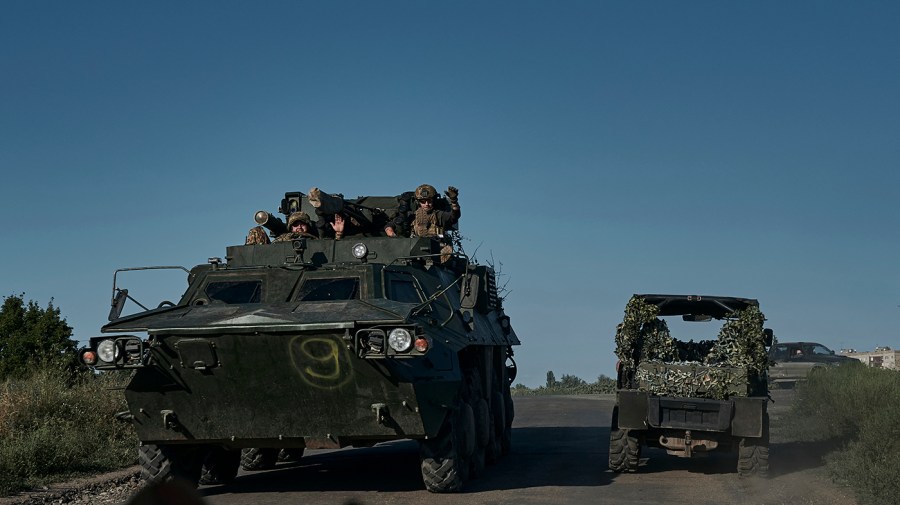 Ukrainian soldiers ride an APC under a clear blue sky