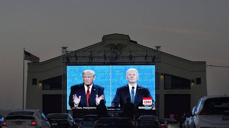 FILE - Elizabeth Allin, bottom center left, and Gideon Lett sit in a convertible while watching President Donald Trump, on left of video screen, and Democratic presidential candidate former Vice President Joe Biden speak during a Presidential Debate Watch Party at Fort Mason Center in San Francisco, Thursday, Oct. 22, 2020. (AP Photo/Jeff Chiu, File)