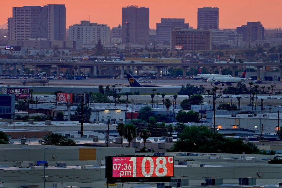 FILE - A sign displays an unofficial temperature as jets taxi at Sky Harbor International Airport at dusk, July 12, 2023, in Phoenix. (AP Photo/Matt York, File)