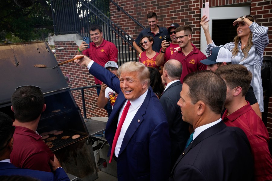 Former President Donald Trump holds a spatula with a hamburger on it as he works the grill during a stop at the Alpha Gamma Rho, agricultural fraternity, at Iowa State University before an NCAA college football game between Iowa State and Iowa, Saturday, Sept. 9, 2023, in Ames, Iowa. (AP Photo/Charlie Neibergall)