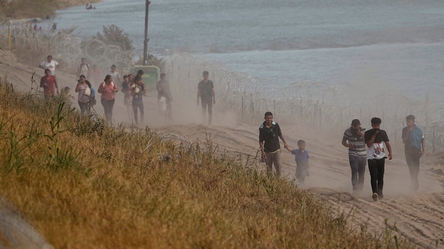 Migrants who crossed the Rio Grande from Mexico to the U.S. kick up dust as they walk along concertina wire, Monday, July 31, 2023, in Eagle Pass, Texas.