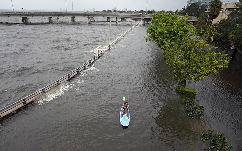 Flood waters pushed by Hurricane Idalia pour over the sea wall along Old Tampa Bay as paddle boarder Zeke Pierce, of Tampa, rides