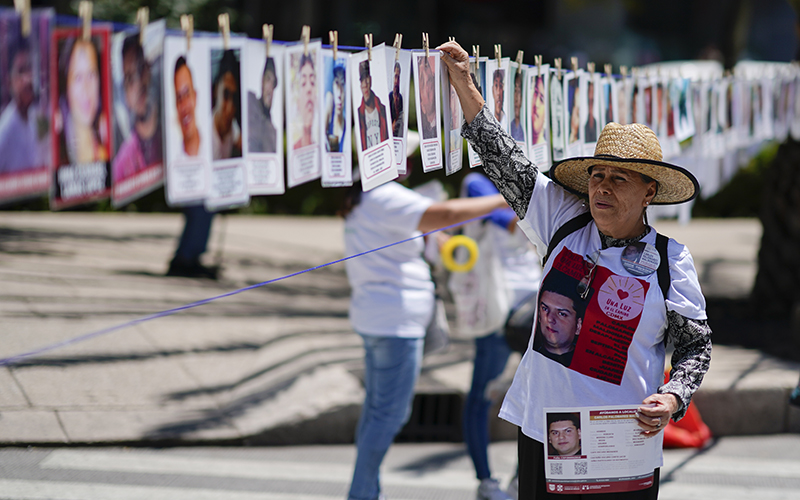 A woman hangs a portrait of a missing person on a line that displays photos and names of other missing people in Mexico