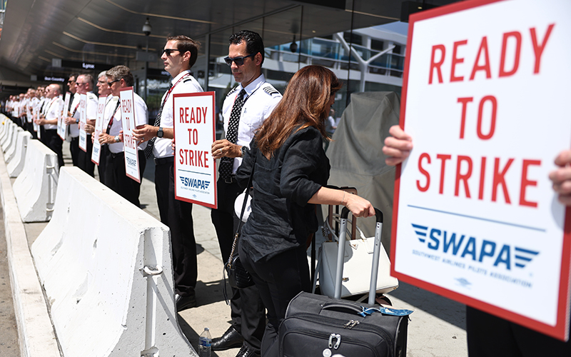 A traveler walks past members of the Southwest Airlines Pilots Association conducting an informational picket over contract negotiations. The protesters are holding signs that read "READY TO STRIKE"