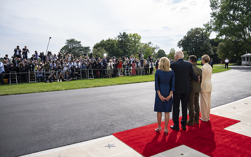 President Biden and first lady Jill Biden welcome Ukrainian President Volodymyr Zelensky and his wife Olena Zelenska to the White House. The photo is taken from behind the four people as they pose for a photo. Across from the foursome, behind a rope, stands a group of photographers .