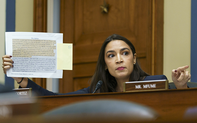 Rep. Alexandria Ocasio-Cortez (D-N.Y.) is seen holding up a piece of paper with a text on it, part of which is highlighted. She is looking intensely toward someone unseen off to the right, and pointing in that direction.