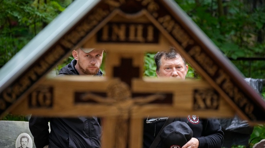 Two men are seen standing through a wooden cross at the grave of Wagner Group's chief Yevgeny Prigozhin