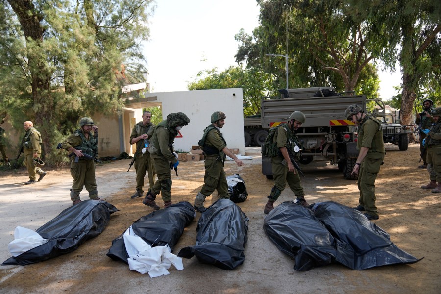 Israeli soldiers stand next to the bodies of Israelis killed by Hamas militants in kibbutz Kfar Azza on Tuesday, Oct. 10, 2023. Hamas militants overran Kfar Azza on Saturday, where many Israelis were killed and taken captive. (AP Photo/Ohad Zwigenberg)