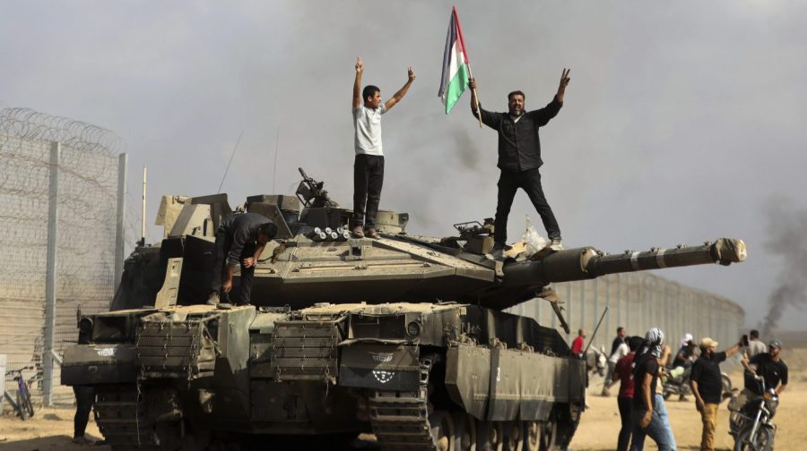 Palestinians wave their national flag and celebrate by a destroyed Israeli tank at the Gaza Strip fence east of Khan Younis southern Saturday, Oct. 7, 2023.