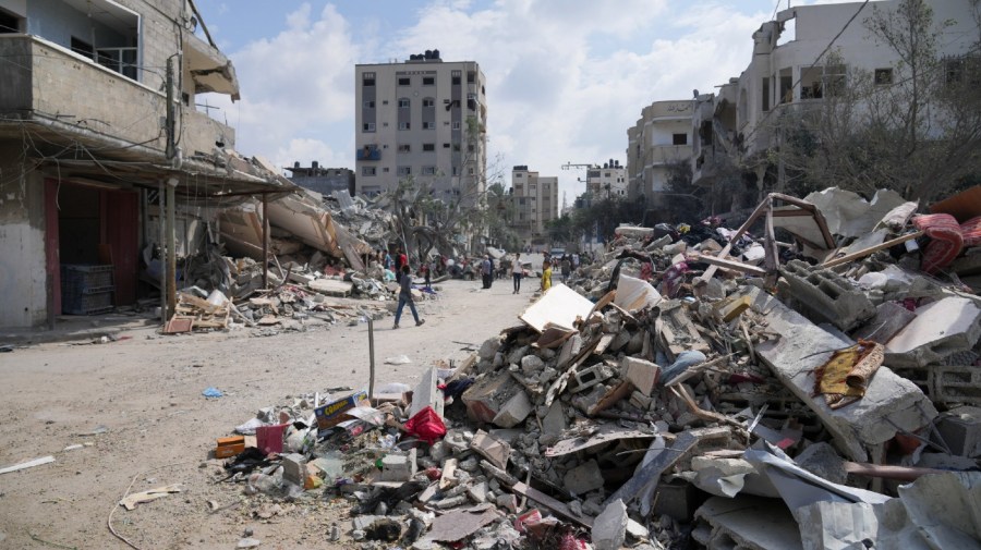 Palestinians walk by buildings destroyed in Israeli airstrikes in Nuseirat camp in the central Gaza Strip, Monday, Oct. 16, 2023.