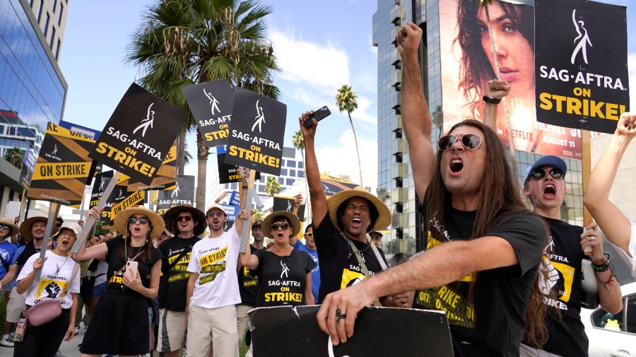 SAG-AFTRA member John Schmitt, second from right, and others carry signs on the picket line outside Netflix on Wednesday, Sept. 27, 2023, in Los Angeles. Hollywood's writers strike was declared over Tuesday night when board members from their union approved a contract agreement with studios, bringing the industry at least partly back from a historic halt in production.