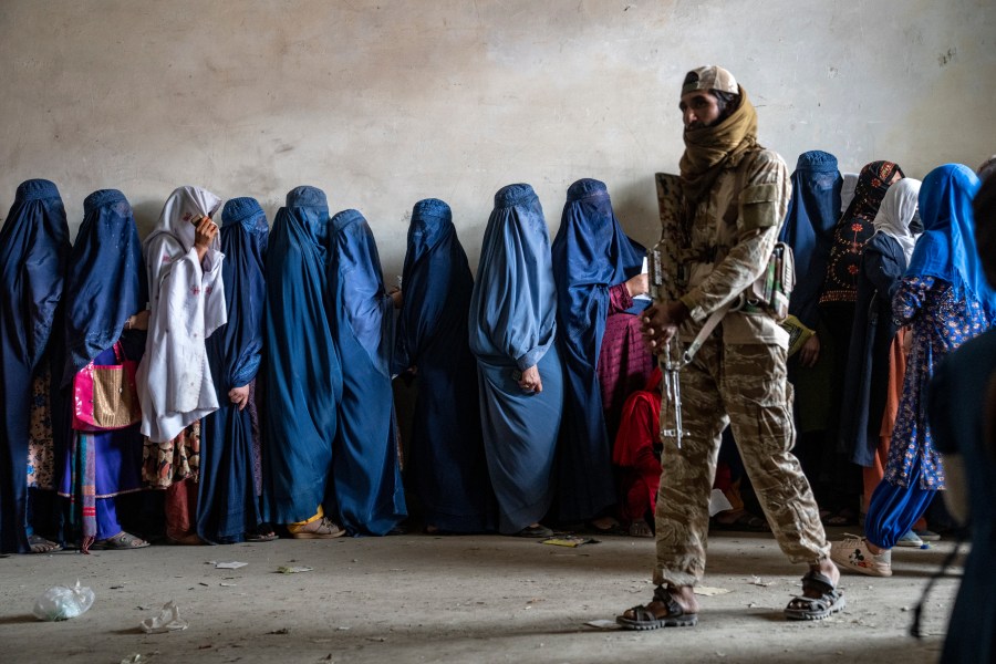 FILE - A Taliban fighter stands guard as women wait to receive food rations distributed by a humanitarian aid group, in Kabul, Afghanistan, on May 23, 2023. Online abuse and hate speech targeting politically active women in Afghanistan has significantly increased since the Taliban took over the country in Aug. 2021, according to a report released Monday, Nov. 20, 2023 by a U.K.-based rights group. (AP Photo/Ebrahim Noroozi, File)