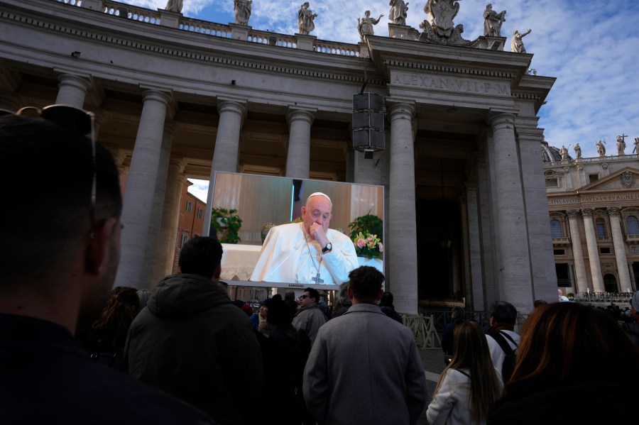 A giant screen broadcasts Pope Francis coughing during the Angelus noon prayer, from the chapel of the hotel at the Vatican grounds where he lives, Sunday, Nov. 26, 2023. Pope Francis says he has a lung inflammation but will go later this week to Dubai for the climate change conference. Francis skipped his weekly Sunday appearance at a window overlooking St. Peter's Square, a day after the Vatican said he was suffering from a mild flu. (AP Photo/Alessandra Tarantino)