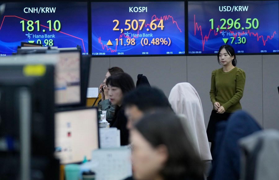 A currency trader passes by the screens showing the Korea Composite Stock Price Index (KOSPI), center, and the foreign exchange rate between U.S. dollar and South Korean won, right, at the foreign exchange dealing room of the KEB Hana Bank headquarters in Seoul, South Korea, Tuesday, Nov. 28, 2023. Shares were mixed in Asia on Tuesday after Wall Street benchmarks edged lower as investors waited for updates on inflation and how American consumers are feeling about the economy. (AP Photo/Ahn Young-joon)