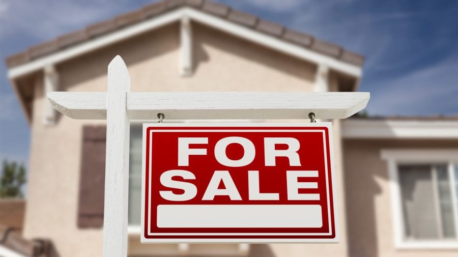 A red for sale sign is seen posted infant of a single-family home.