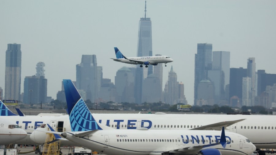 United Airlines planes are seen at an airport as another one lands in the distance.